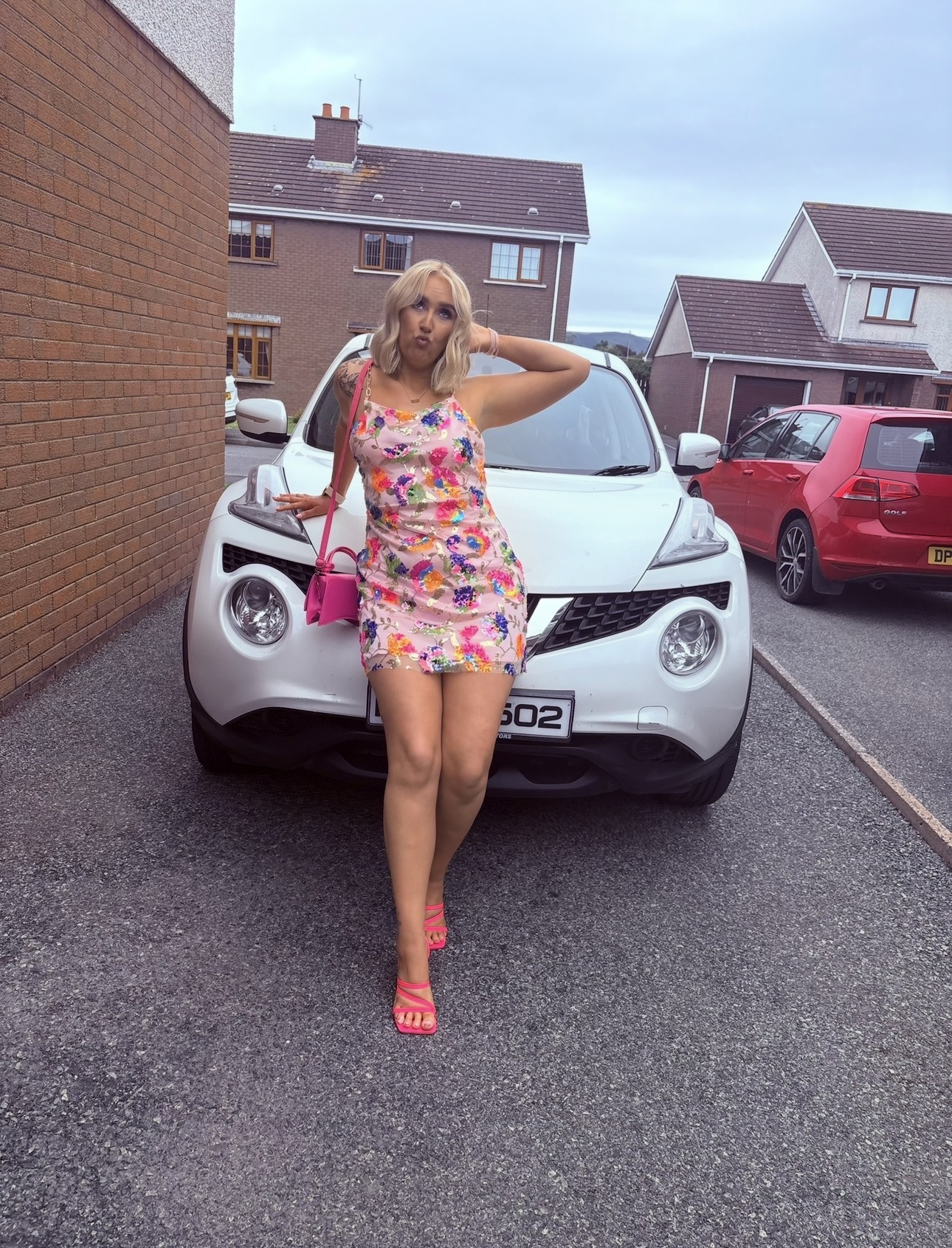 Rebecca playfully posing in a floral dress and pink heels in the driveway